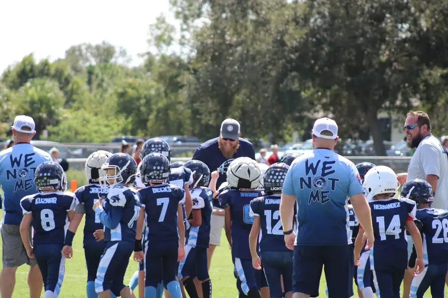 Bobcats coaches wearing We Not Me shirts leading the team huddle