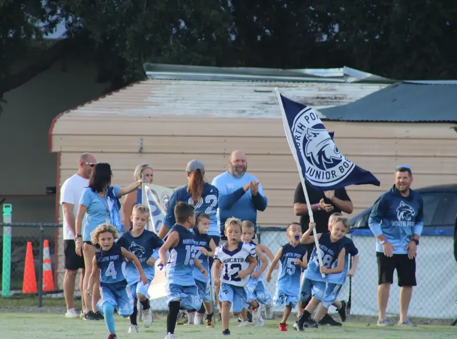 Young Bobcats charging onto the field with the team flag as parents cheer