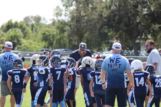 Bobcats coaches wearing We Not Me shirts leading the team huddle